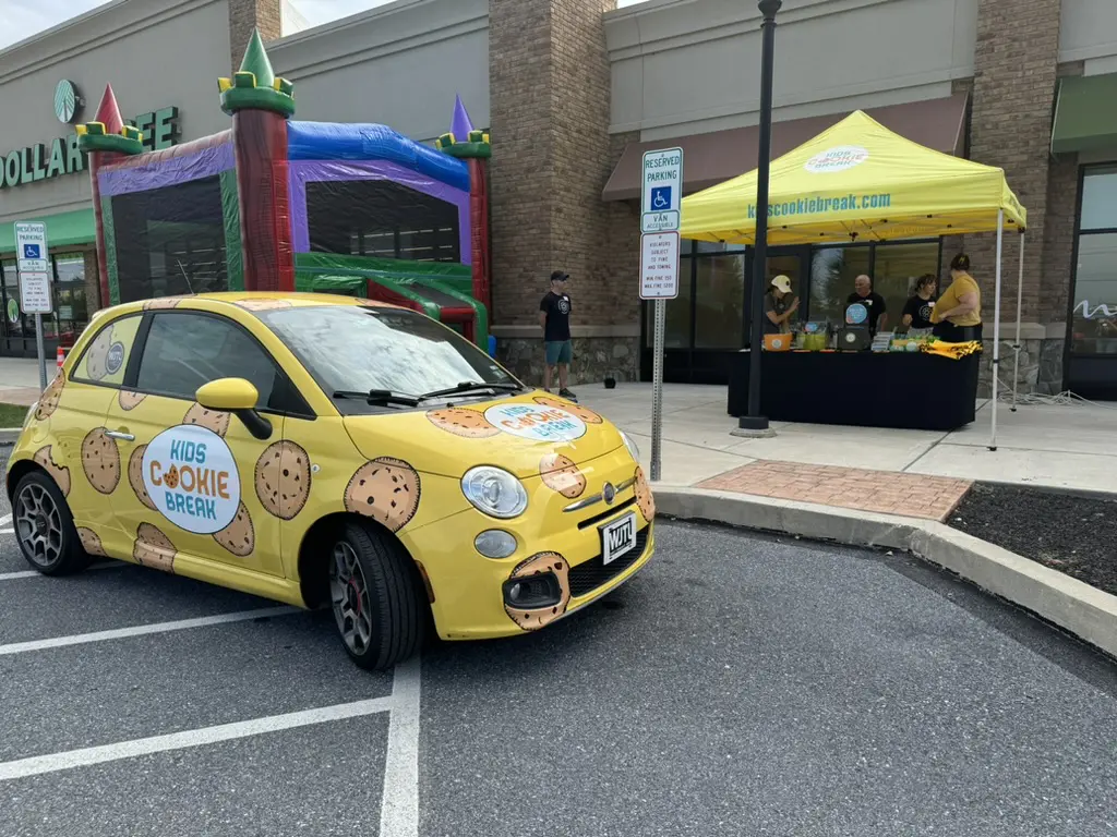 A yellow car covered in a decal for "Kid's Cookie Break"