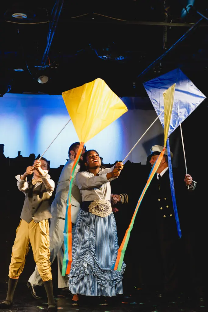 Children cast members from Mary Poppins smiling and performing during a kite flying scene.