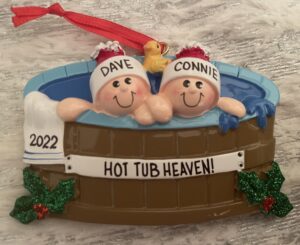 A Christmas ornament from 2022 with two people wearing santa hats labeled Dave and Connie sitting in a hot tub.